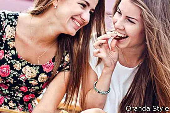 Kaks noort naissõpra naeravad ja söövad õues šokolaadi