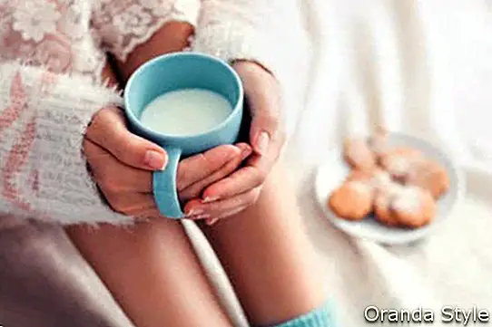Мека снимка на жена на леглото с чаша мляко в ръце