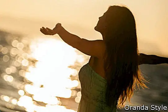Pekná mladá žena sa teší na západ slnka na pláži s rukami dokorán