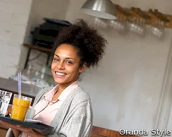 Portrét usmívající se servírka drží tác s nápoji v restauraci