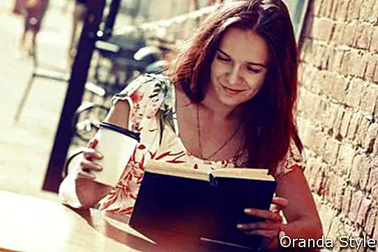 naeratav tüdruk istub tänaval suveterrassil koos hommikukohvi ja raamatu lugemisega