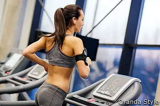 wanita dengan telefon pintar atau pemain dan fon telinga yang bersenam di treadmill di gym