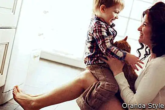 Māte ar savu bērnu spēlējas ar mājdzīvnieku uz grīdas pie virtuves mājās