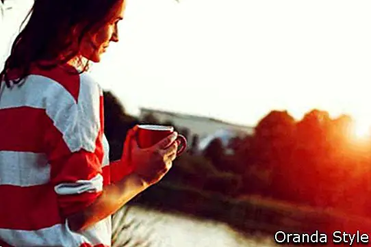 hezká dívka s ranní kávou při východu řeky