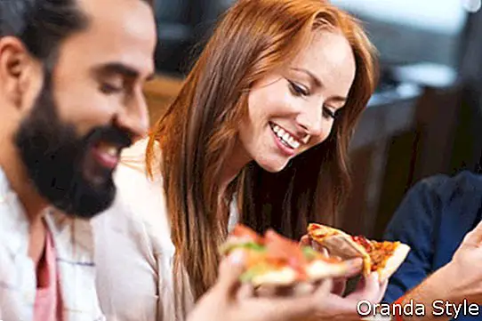पिज्जा खाते हुए मुस्कुराते हुए दोस्त और रेस्तरां में बीयर पीते हुए