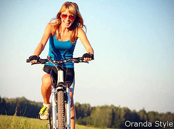 Χαμογελαστή γυναίκα με κόκκινα γυαλιά ιππασίας σε ένα ποδήλατο σε έναν επαρχιακό δρόμο