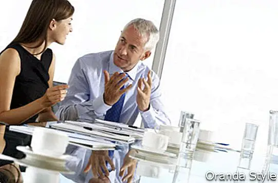 अनौपचारिक चर्चा वाले बोर्डरूम टेबल के आसपास बैठे दो बिजनेस कोलाइग्स