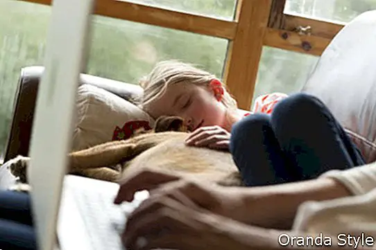 Frau, die einen Laptop mit ihrer Tochter und Schoßhund zusammen schlafen nahe bei ihr verwendet