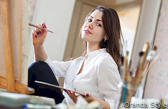 Smaidoša meitene darbnīcā glezno audeklu ar eļļas krāsām
