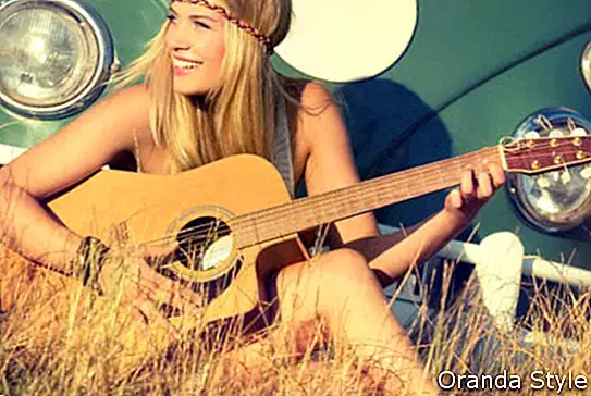 젊은 여자는 필드에 앉아서 기타 연주