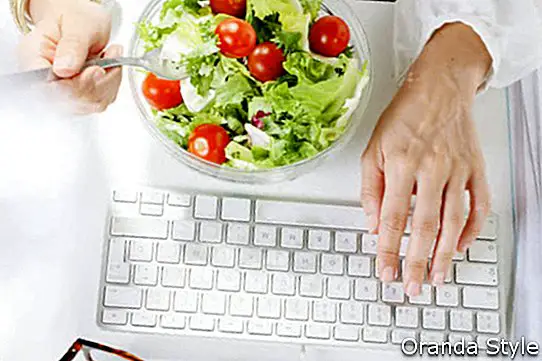 Pakar perniagaan muda makan salad semasa bekerja di pejabat