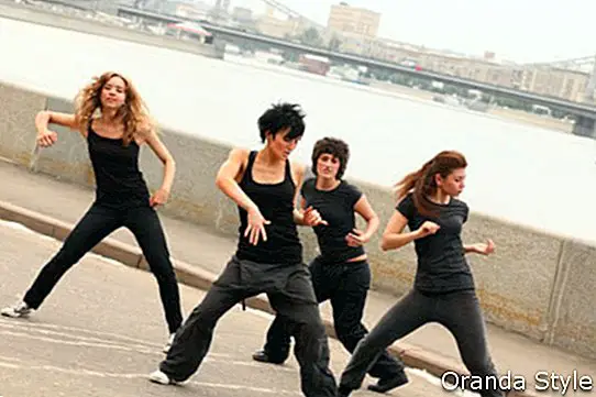 Neljä tyttöä samoissa mustissa vaatteissa tanssii pengerrys sillan taustalla