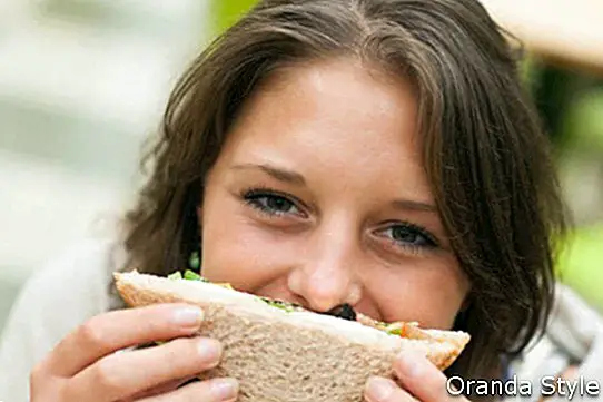 усмихната студентка със сандвич в кафенето
