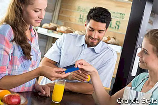 Seitenansicht eines Paares, das Rechnung an der Kaffeestube unter Verwendung der Kartenrechnung zahlt