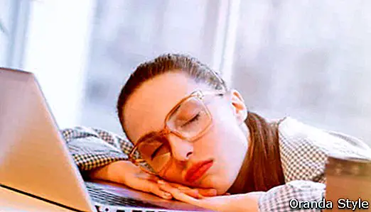 väsynyt ja uupunut freelance-nainen nukkuu kannettavalla tietokoneella toimistossa