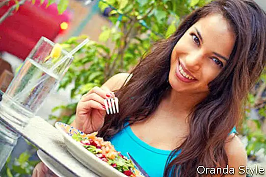 млада привлекателна жена, ядеща салата на маса на кафе
