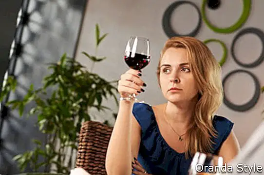 Penkta liūdna moteris su taure vyno, žiūrinti į langą per pasimatymą