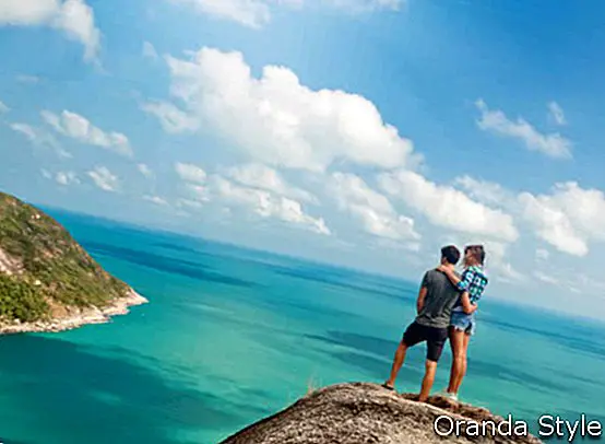 זוג צעירים של מטיילים על גבעה עם נוף מדהים של האוקיאנוס