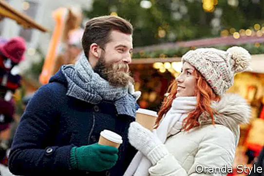 cuplu fericit de turiști în haine calde, care beau cafea din căni de hârtie de unică folosință din orașul vechi