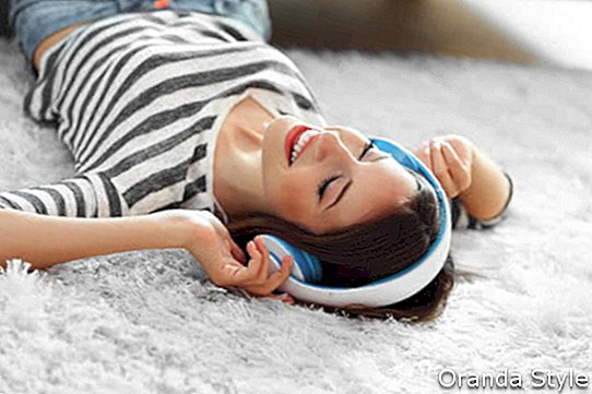 Mujer escuchando música en auriculares en la alfombra en la habitación