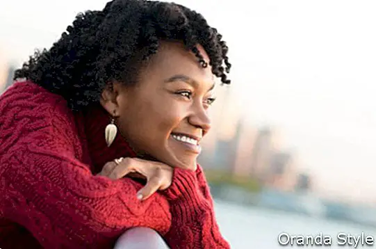 Ciérrese encima del retrato de una mujer africana feliz joven que se inclina en la barandilla de un puente cerca del río