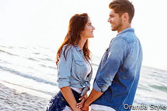 Щастлива млада двойка стои и се държи за ръце на плажа