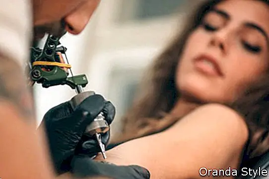 Artis tato membuat tato di lengan anak perempuan