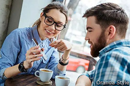 זוג מאושר שמשתמש בסמארטפון יחד ושותים קפה בבית הקפה