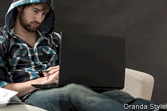 hombre sentado en un sofá mirando una computadora portátil
