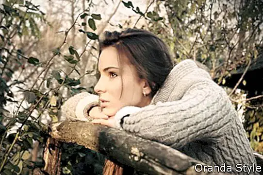 Hermosa mujer inclinada mentón en la vieja valla de madera pensando
