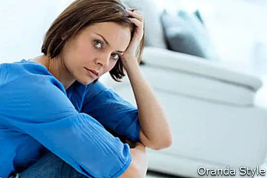 Liūdnos jaunos moters, sėdinčios prie sofos namuose, portretas