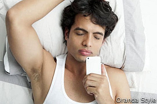 Vīrietis gulēja uz gultas turot mobilo tālruni