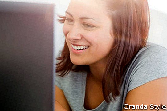 Rõõmus juhuslik naine, kes töötab oma sülearvutiga kodus diivanil lebades