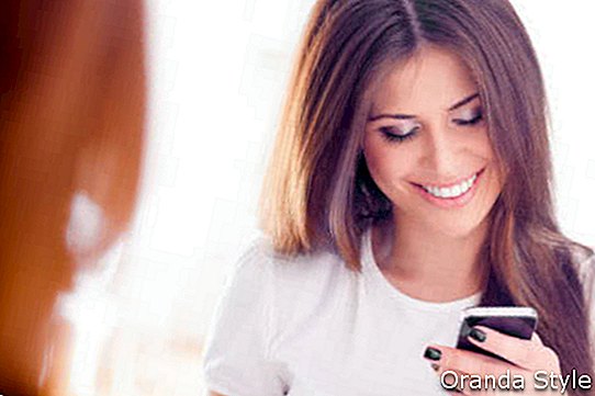 Señora hermosa joven tocando y mirando su teléfono inteligente en casa