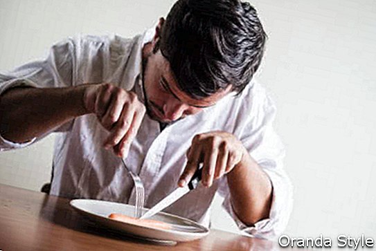 junger stilvoller Mann mit weißem Hemd Karotte hinter einem Tisch essend