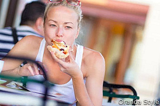 Zufällige blonde Dame, welche die Pizzascheibe im Freien im typischen italienischen Straßenrestaurant am heißen Sommertag isst