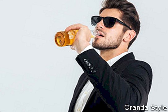 Stilvoller gutaussehender Mann in der Sonnenbrille und im schwarzen Anzug trinkend von der Bierflasche