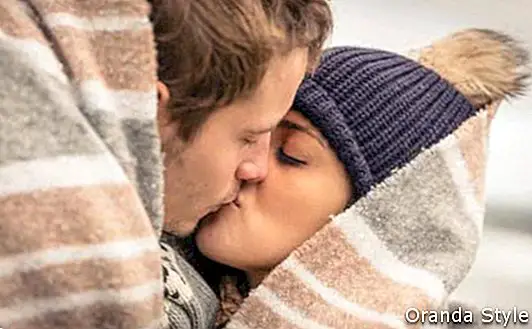 Primer plano de la joven y bella pareja besándose bajo una manta en un día frío