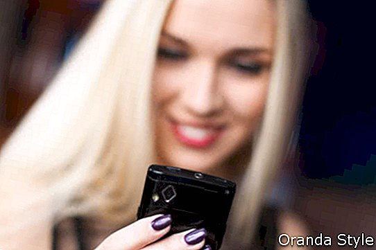 אישה צעירה ויפה, לחייך עם טלפון נייד בבית קפה