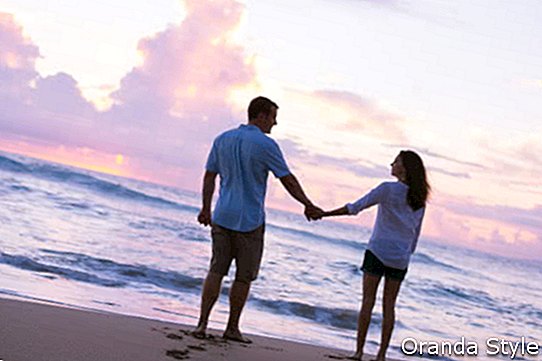 Jovens amantes, caminhando na praia ao pôr do sol em férias tropicais