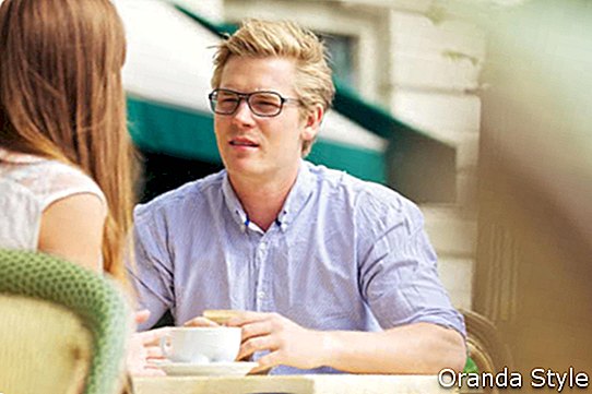 Kjekk blond mann som sitter på utekafé og hører på kjæresten