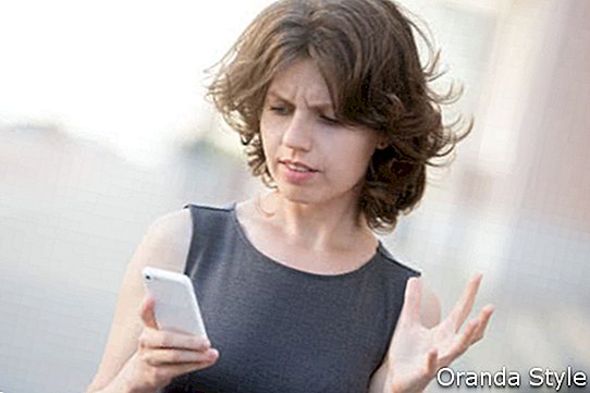 Портрет на млада жена, която държи мобилен телефон в ръцете на улицата през лятото