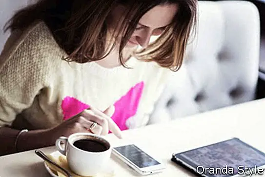 duduk di sebuah kafe dengan secawan kopi dan membaca mesej di telefon dan mencari gambar di tablet
