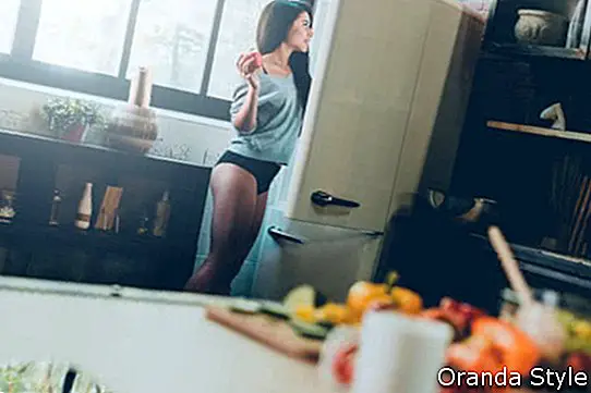 Schöne junge Afrikanerin, die den Kühlschrank untersucht und roten Pfeffer bei in der Küche zu Hause stehen hält