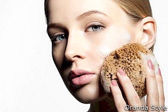Kvinne renser og eksfolierer huden med et naturlig ansiktssvamp av skum