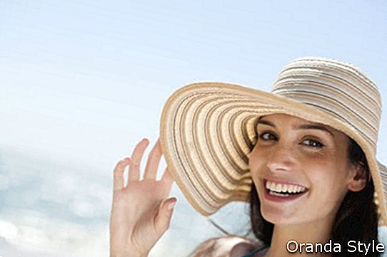portret čudovite mlade ženske v kopalkah na plaži, ki se z velikim klobukom varuje pred soncem
