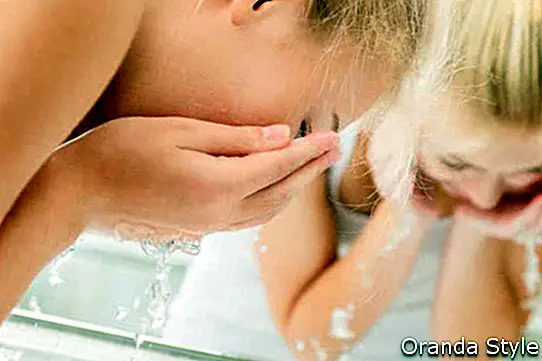 Mlada ženska si umiva obraz s čisto vodo v kopalnici