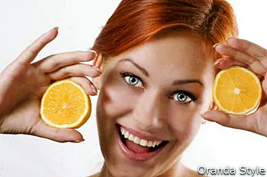 Krásná dívka drží dva šťavnaté citrony poblíž její tváře