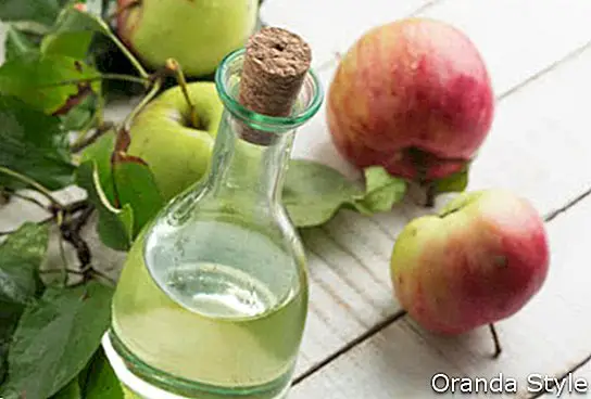 Obuolių actas ir obuoliai ant balto medinio stalo