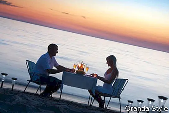 Mladi par dijeli romantičnu večeru uz svijeće i čaše za vino na plaži morskog pijeska